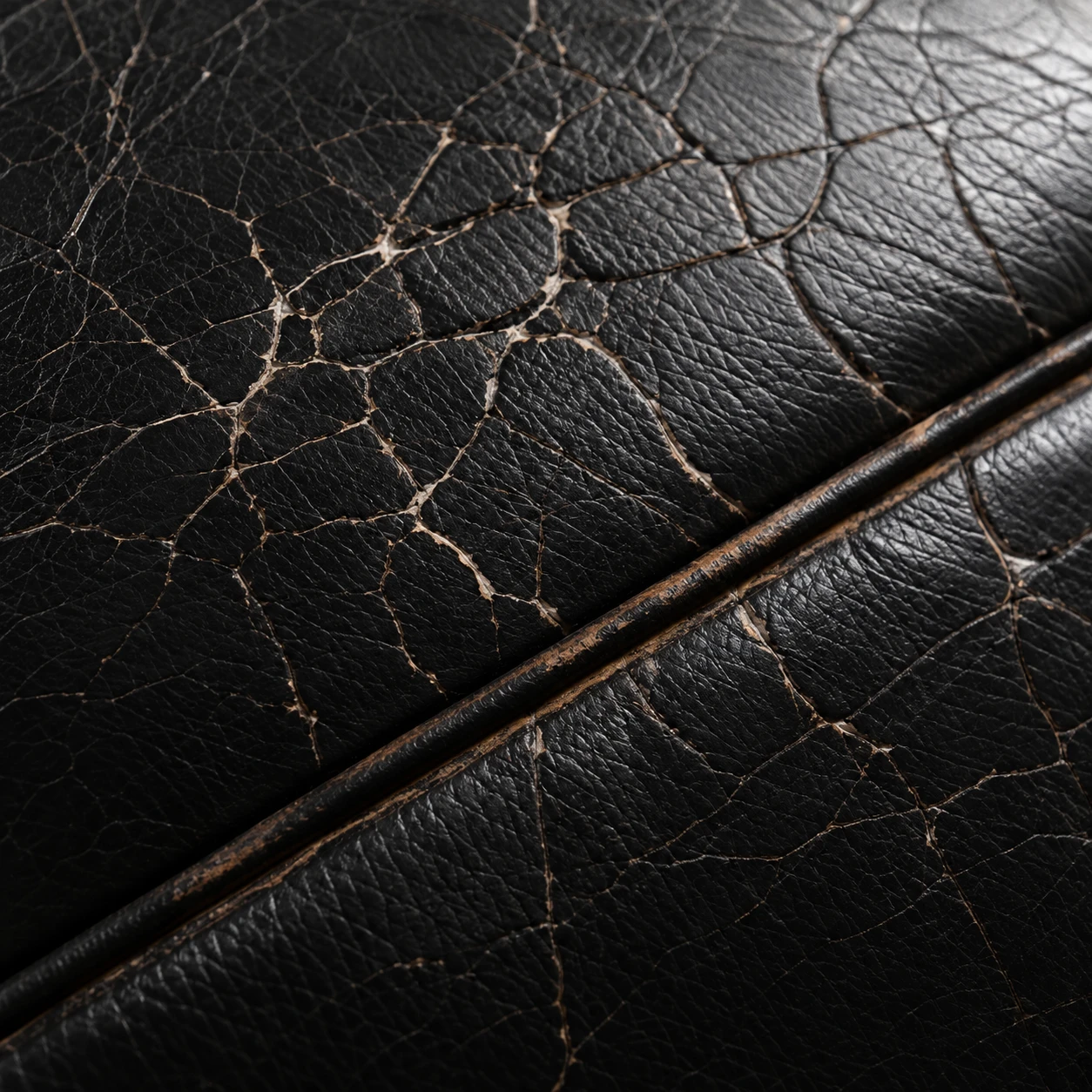 A network of fine cracks spreading across a black leather panel and its seam