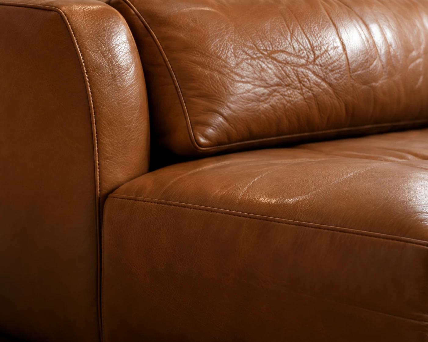 The arm and back cushion of a tan leather sofa