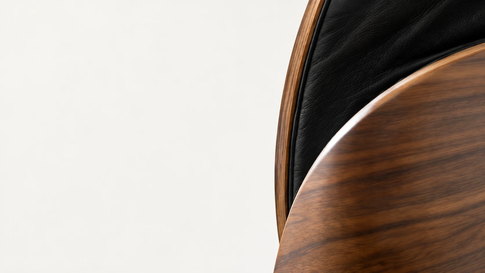 The curved walnut shell and black leather cushion of a lounge chair