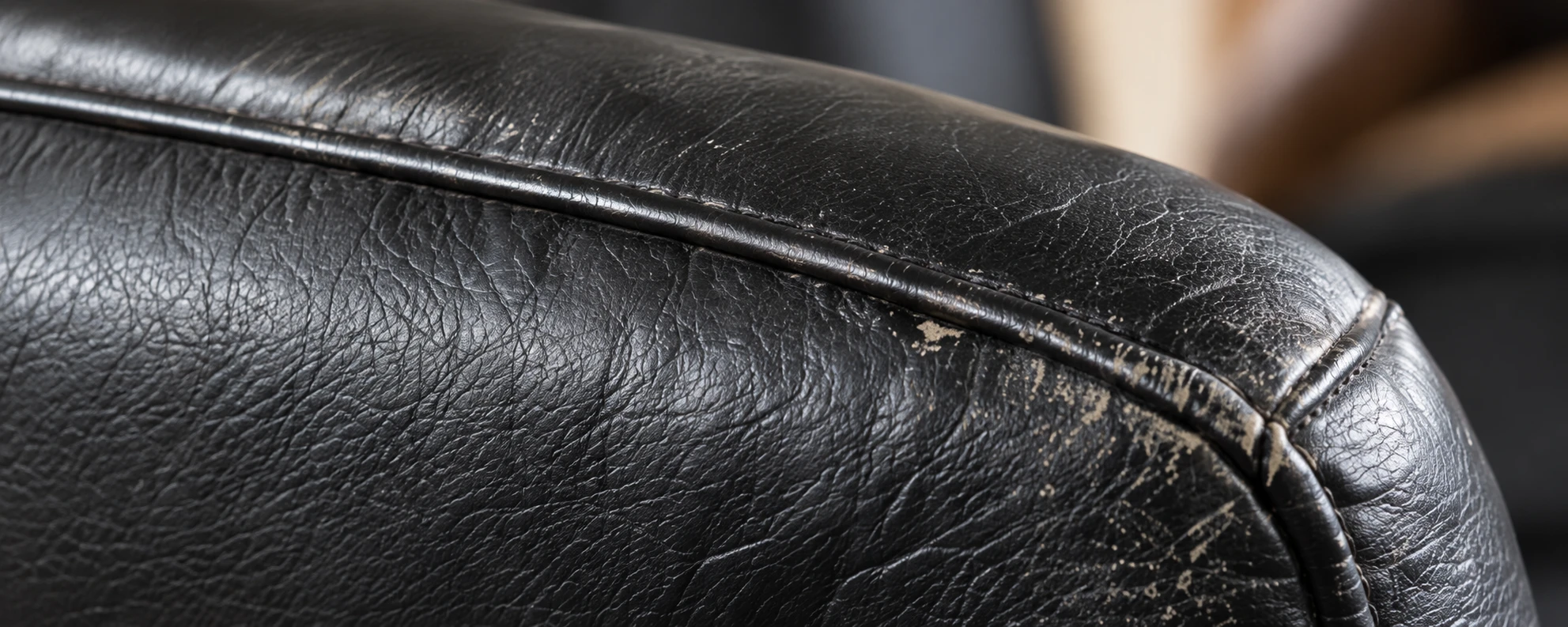 Scuffing and surface wear along the rolled arm of a black leather chair