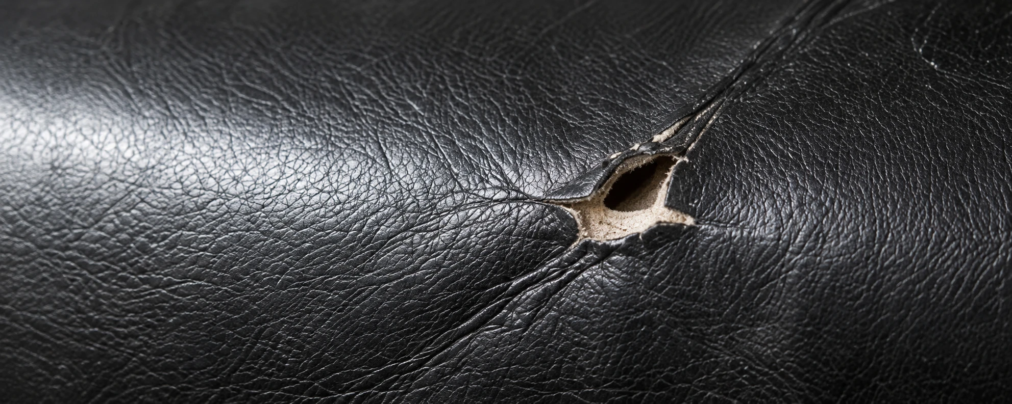 A small torn hole in a black leather panel