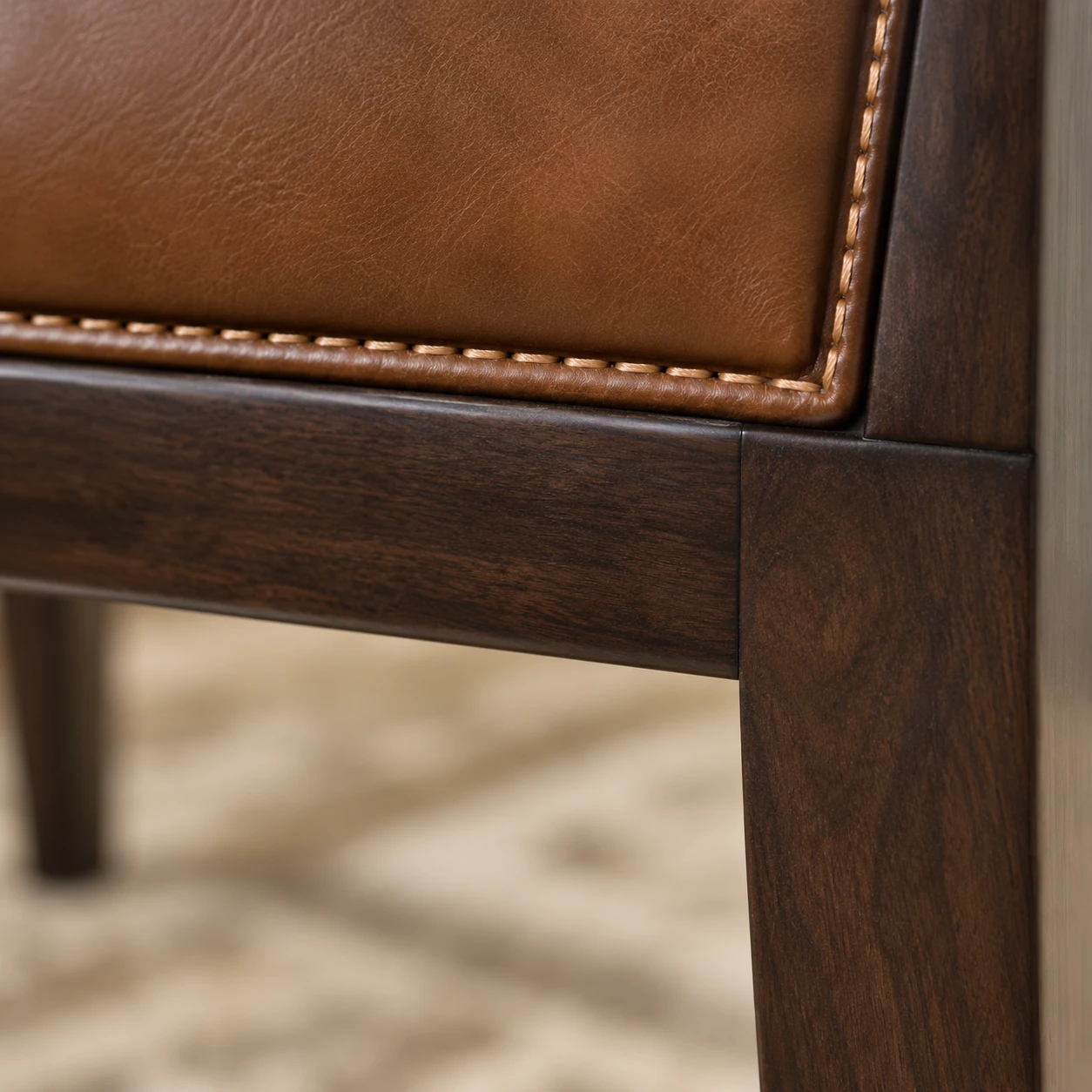 Tan leather stitched along its edge and tucked tight against the dark timber rail and leg of a dining chair