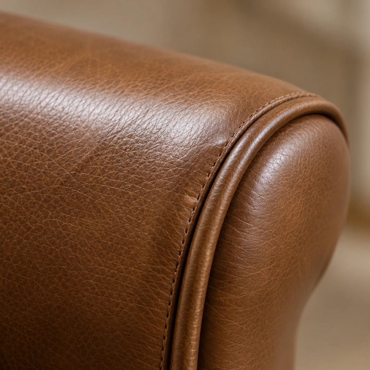 A close view of a tan leather chair back edge finished with a rolled leather piping run along the seam