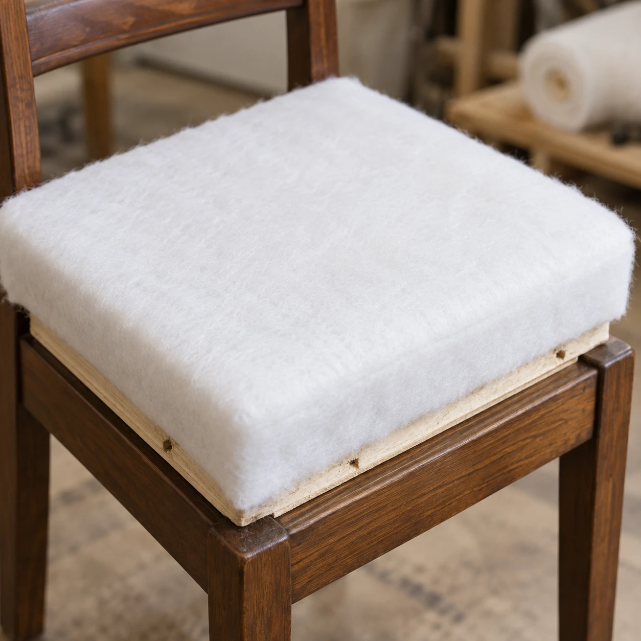 White polyester wadding laid over foam and wrapped down onto a timber seat board fitted in a chair frame