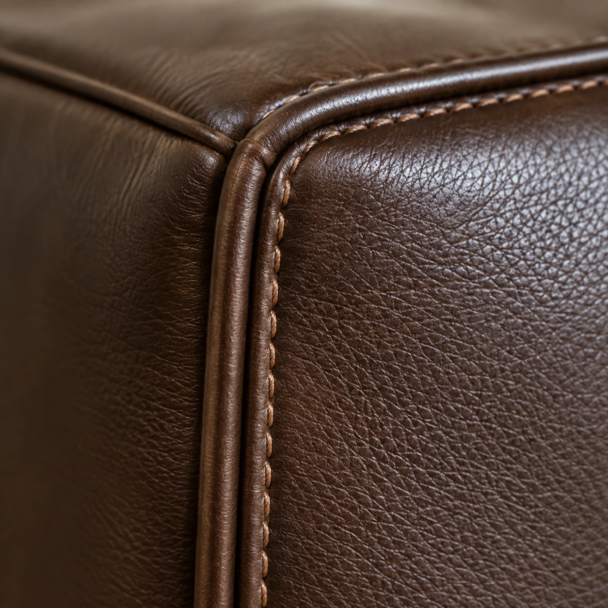 The corner of a dark brown leather chair back where two panels meet in a piped seam with contrast top-stitching