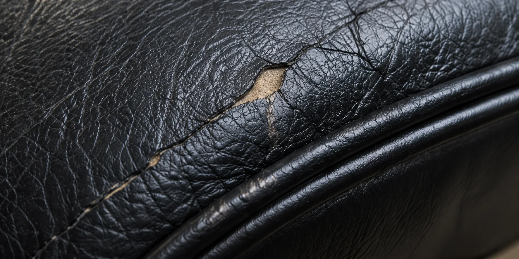 Close-up of cracked black leather beside the piping on an Eames chair