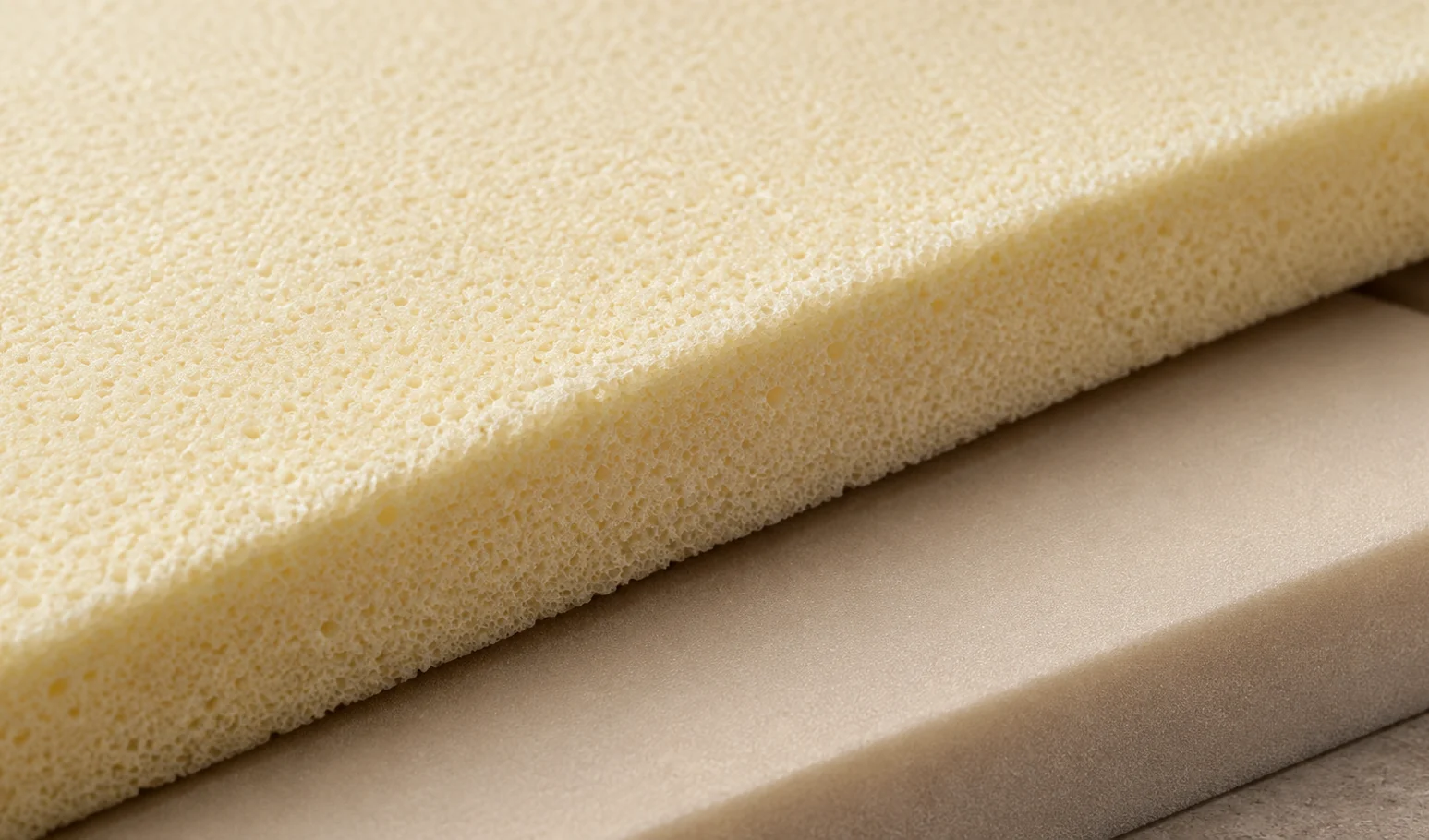 Cut foam slab layered beneath cream upholstery, the cut edge showing the depth