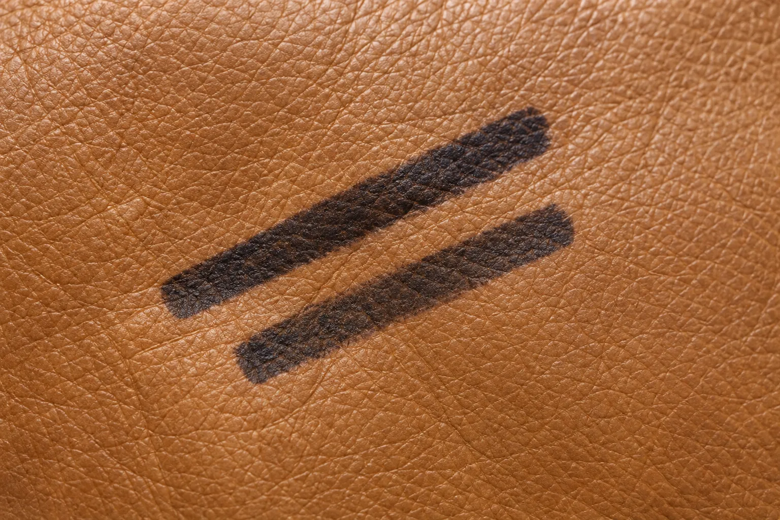 Two thick black marker strokes sitting on the surface of tan leather