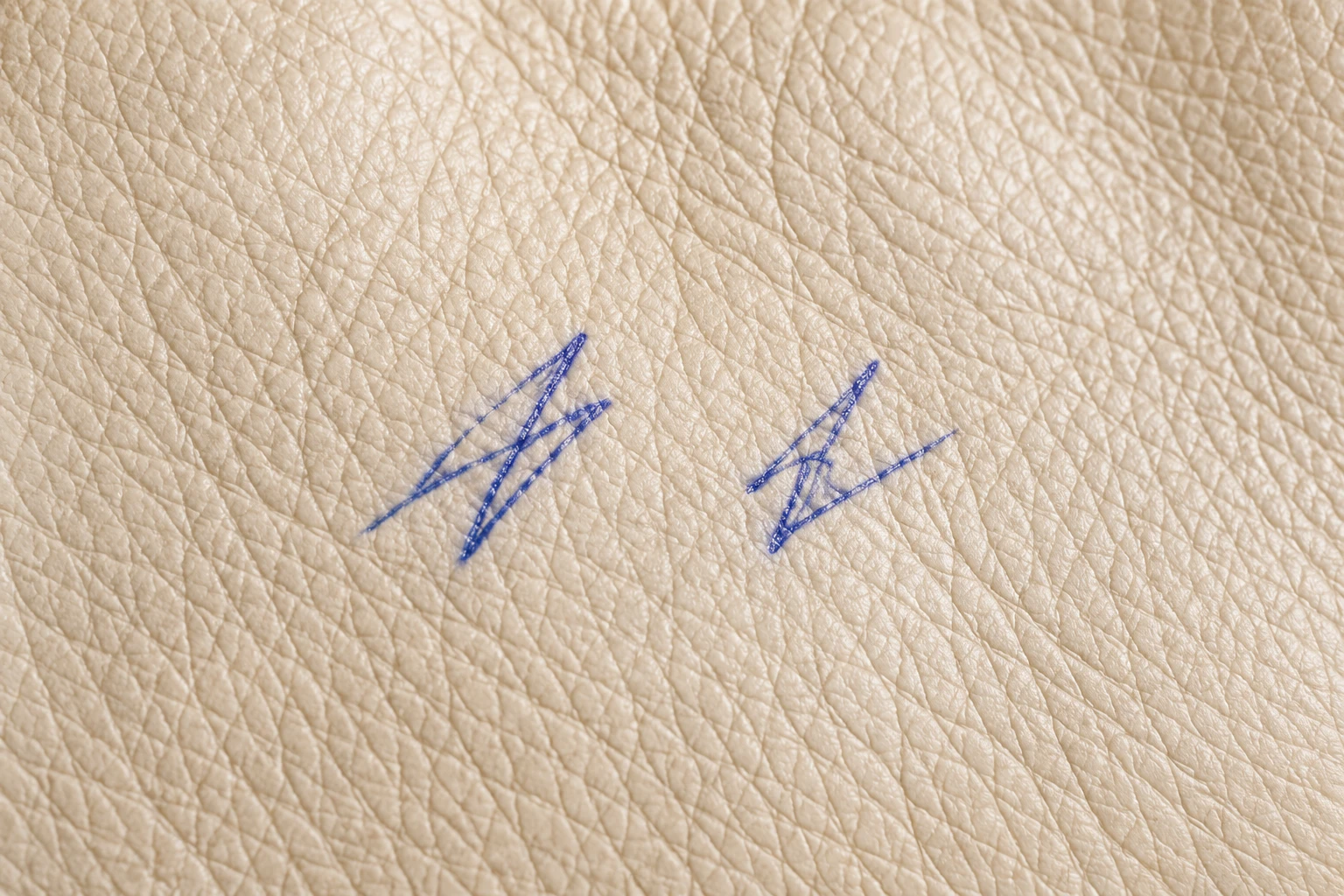 Two small blue pen scribbles side by side on cream leather