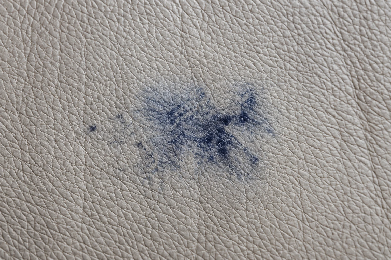 A blue ink smudge rubbed into pale grey leather, spread wide with no clear line