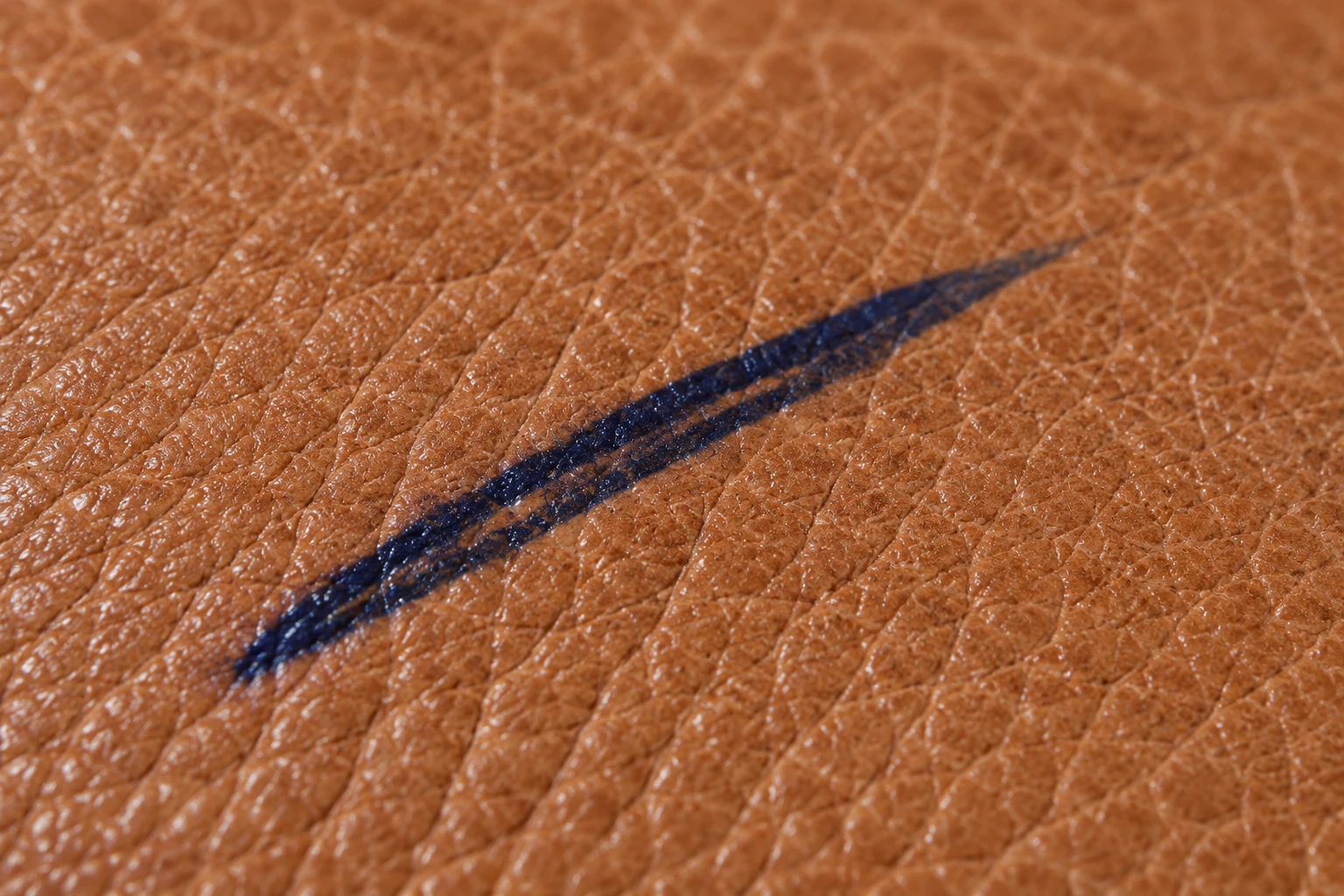 Close-up of a crisp navy ballpoint stroke sitting on top of tan leather grain