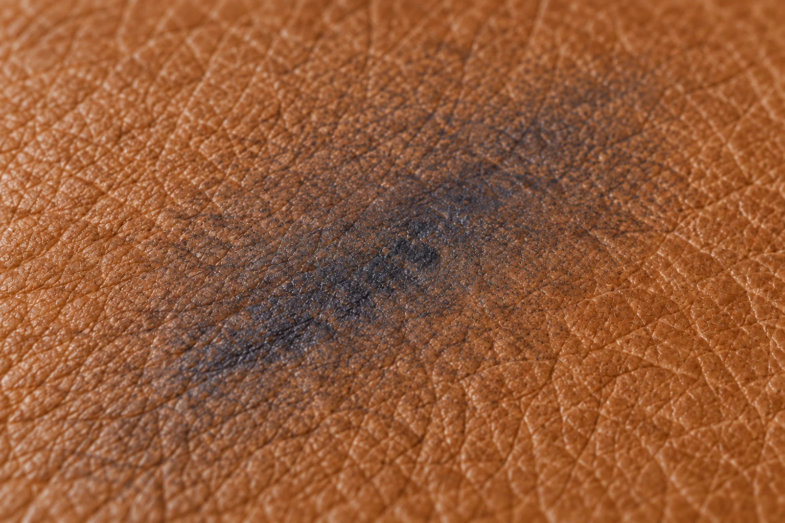 A faint diffuse grey-blue halo sunk into the tan leather grain with no sharp edge left to work to