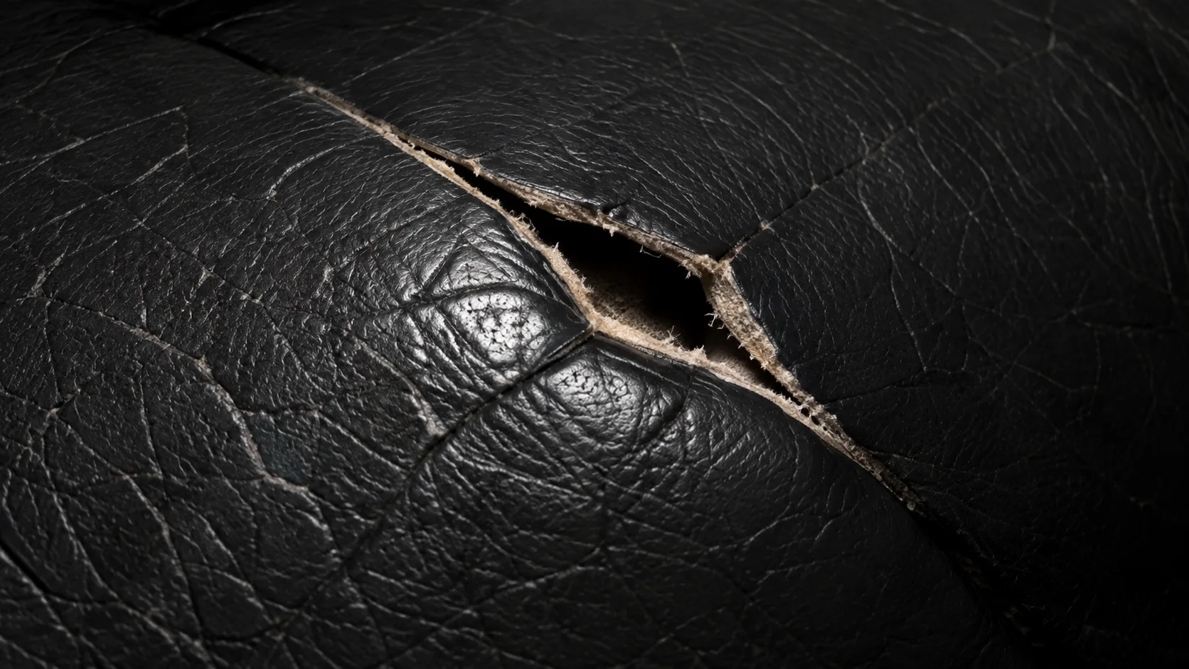 Open tear in dark leather exposing the lighter layer underneath