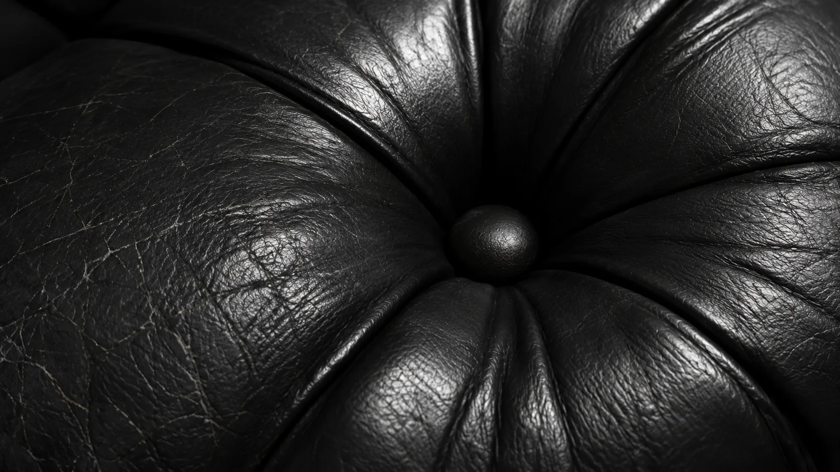 Leather worn smooth and shiny around a tufted button on a seat cushion
