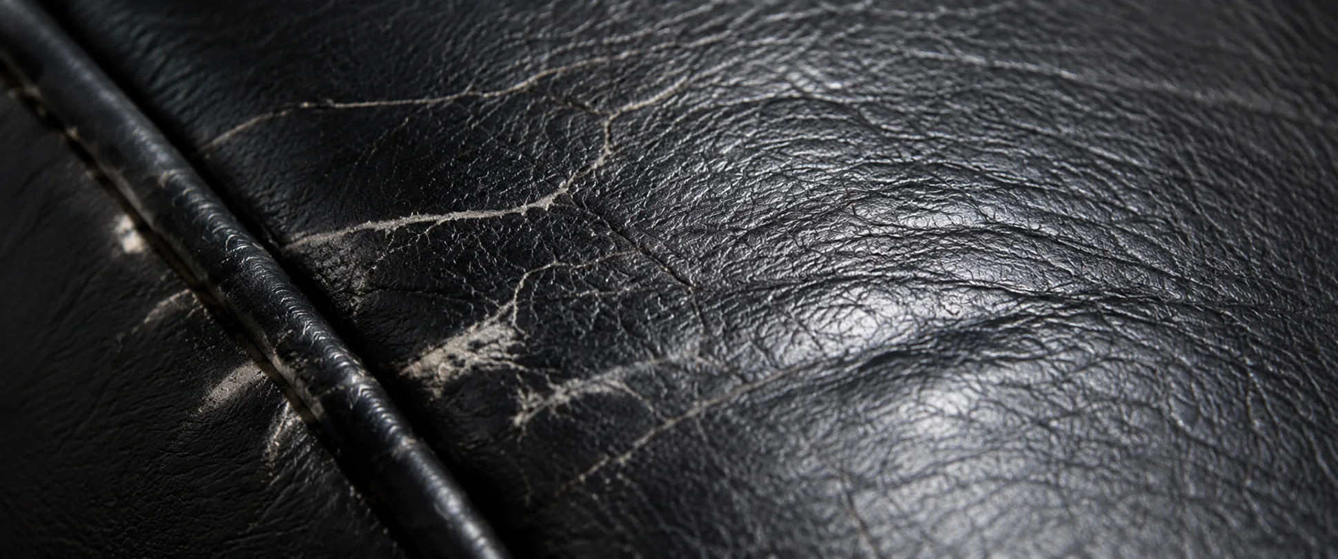 Close-up of cracked black leather beside a piped seam