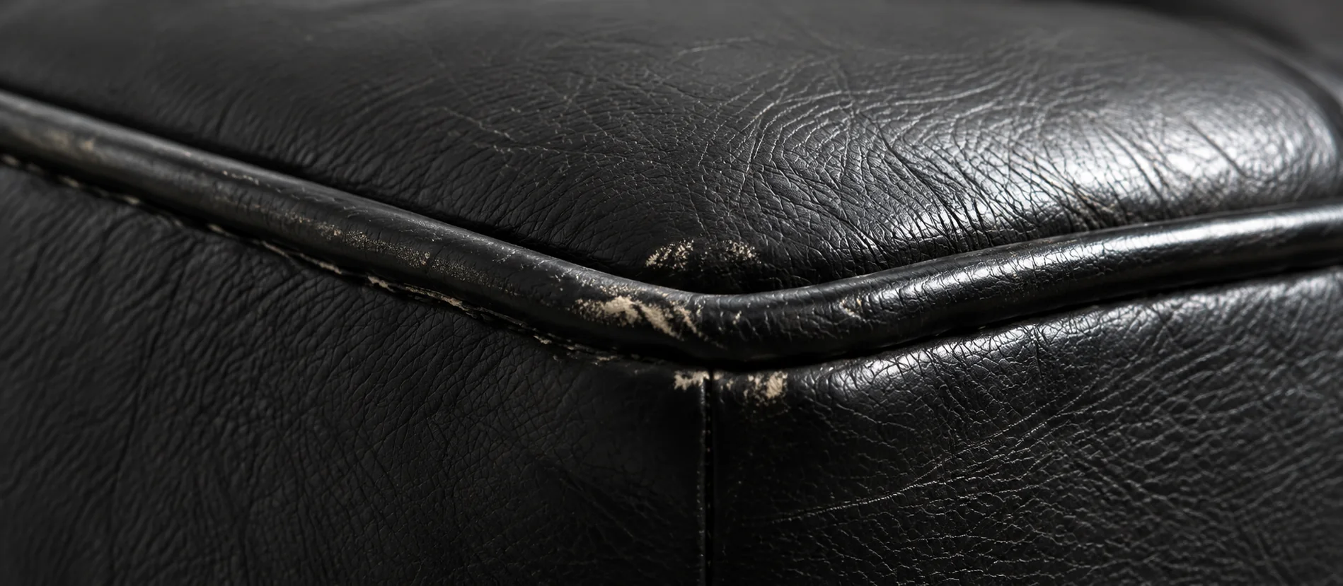 Worn leather piping running along the edge of a black cushion