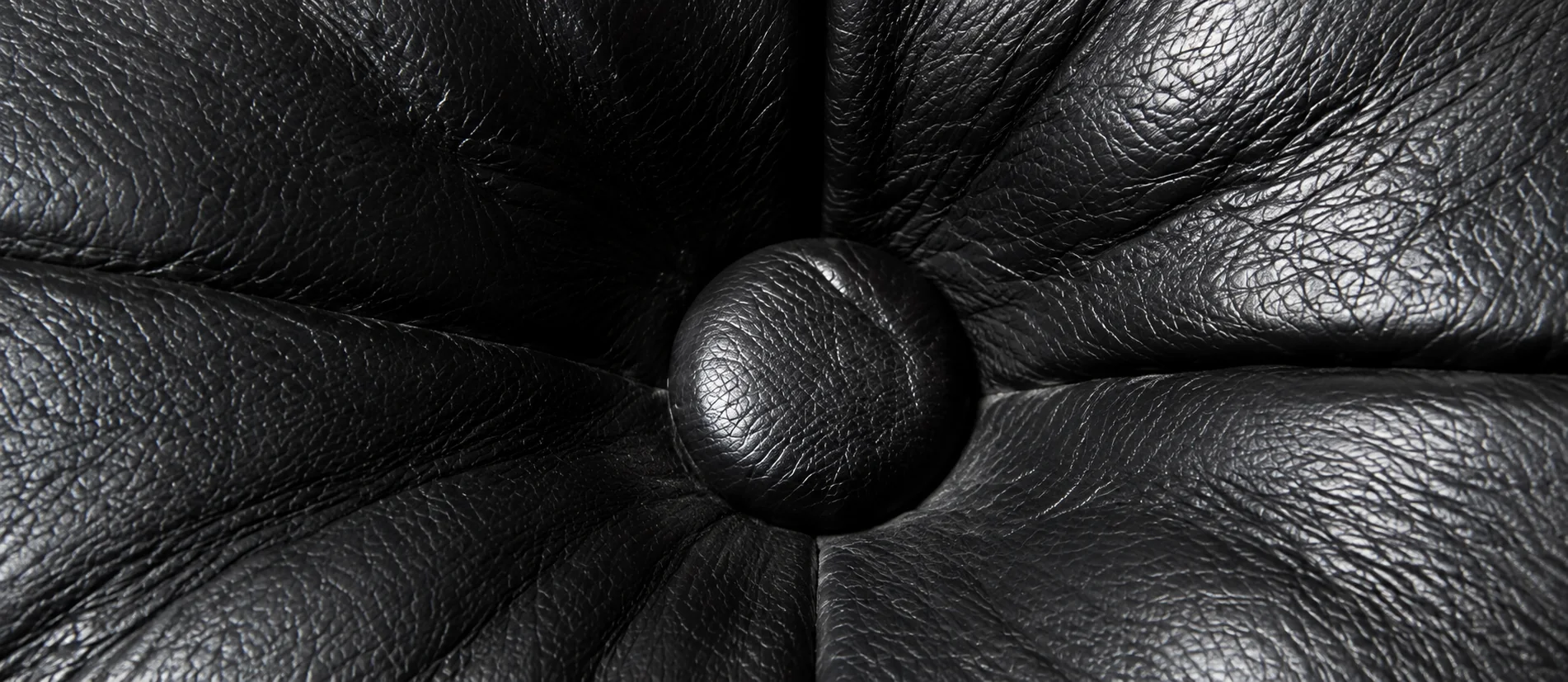 Close-up of a tufted button pulled into a black leather Knoll cushion