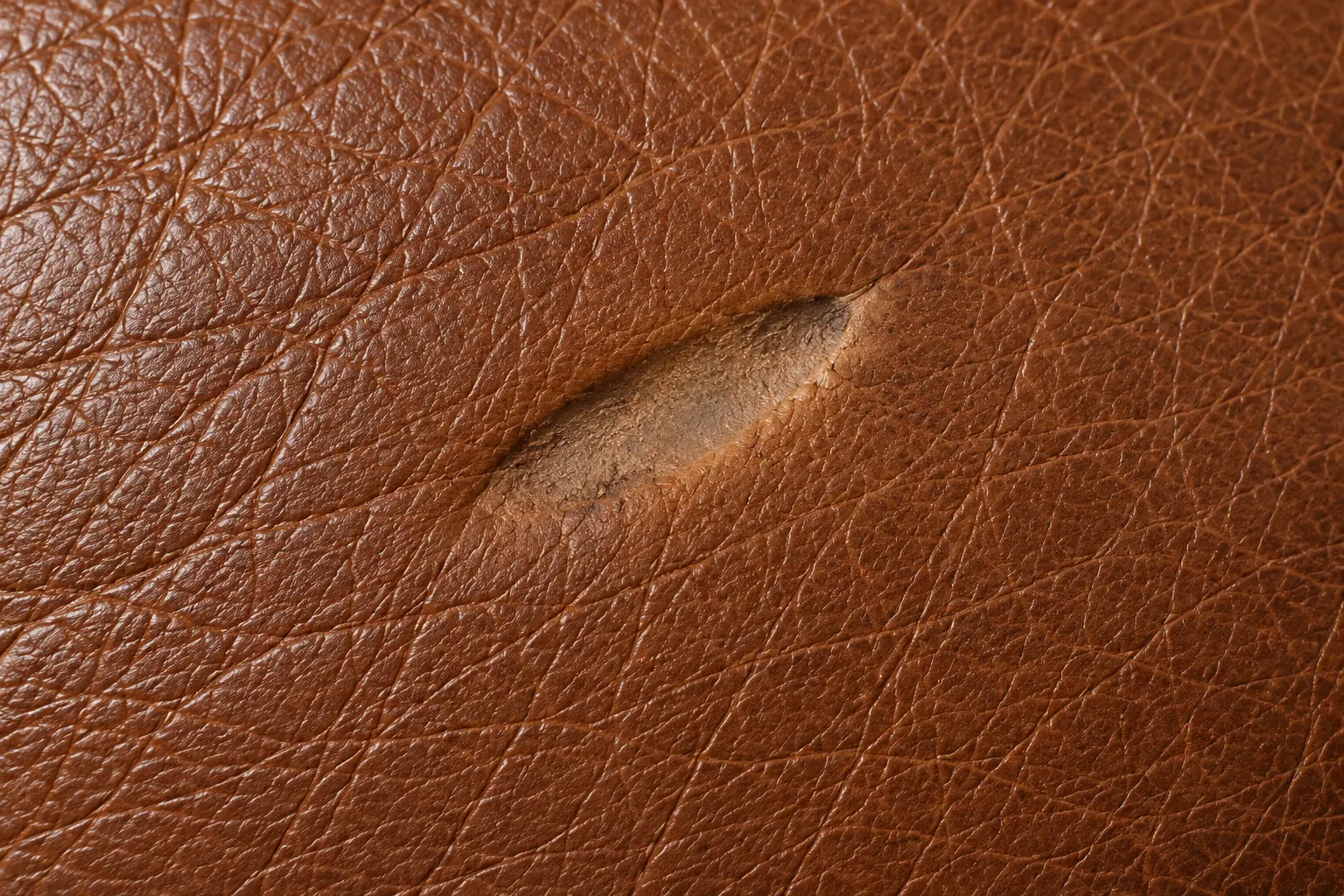 Burn mark on brown leather: the surface is discoloured and flattened but still closed