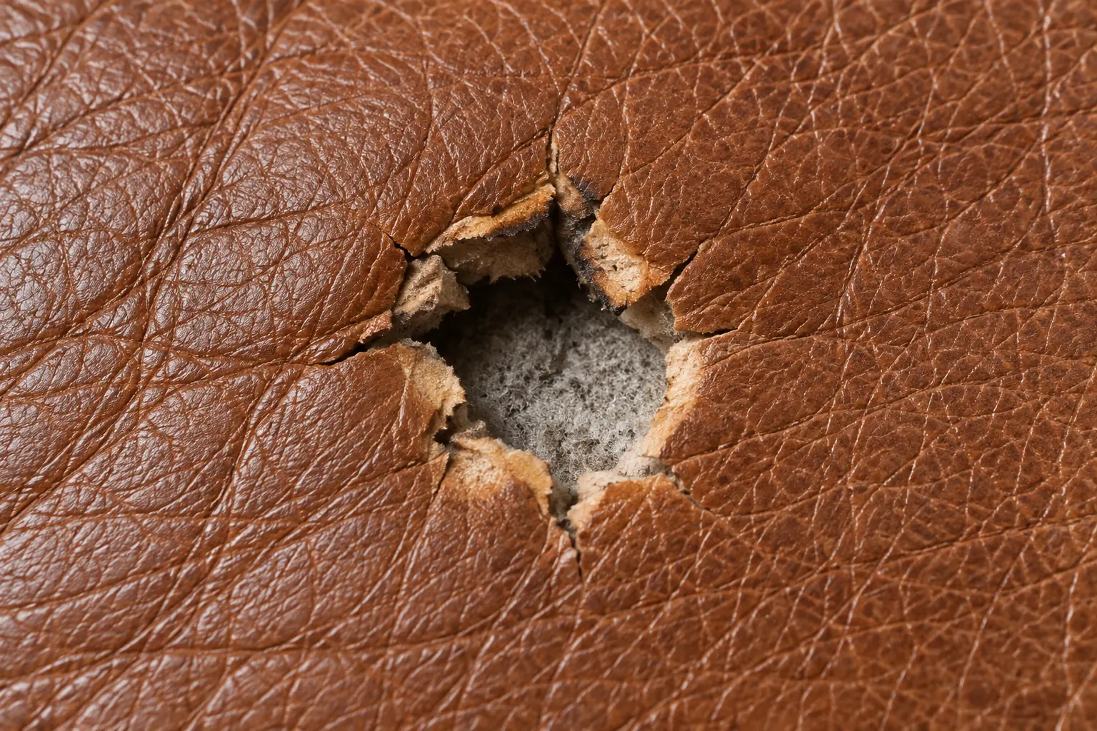 Surface burn on brown leather with the top layer broken back to pale fibre