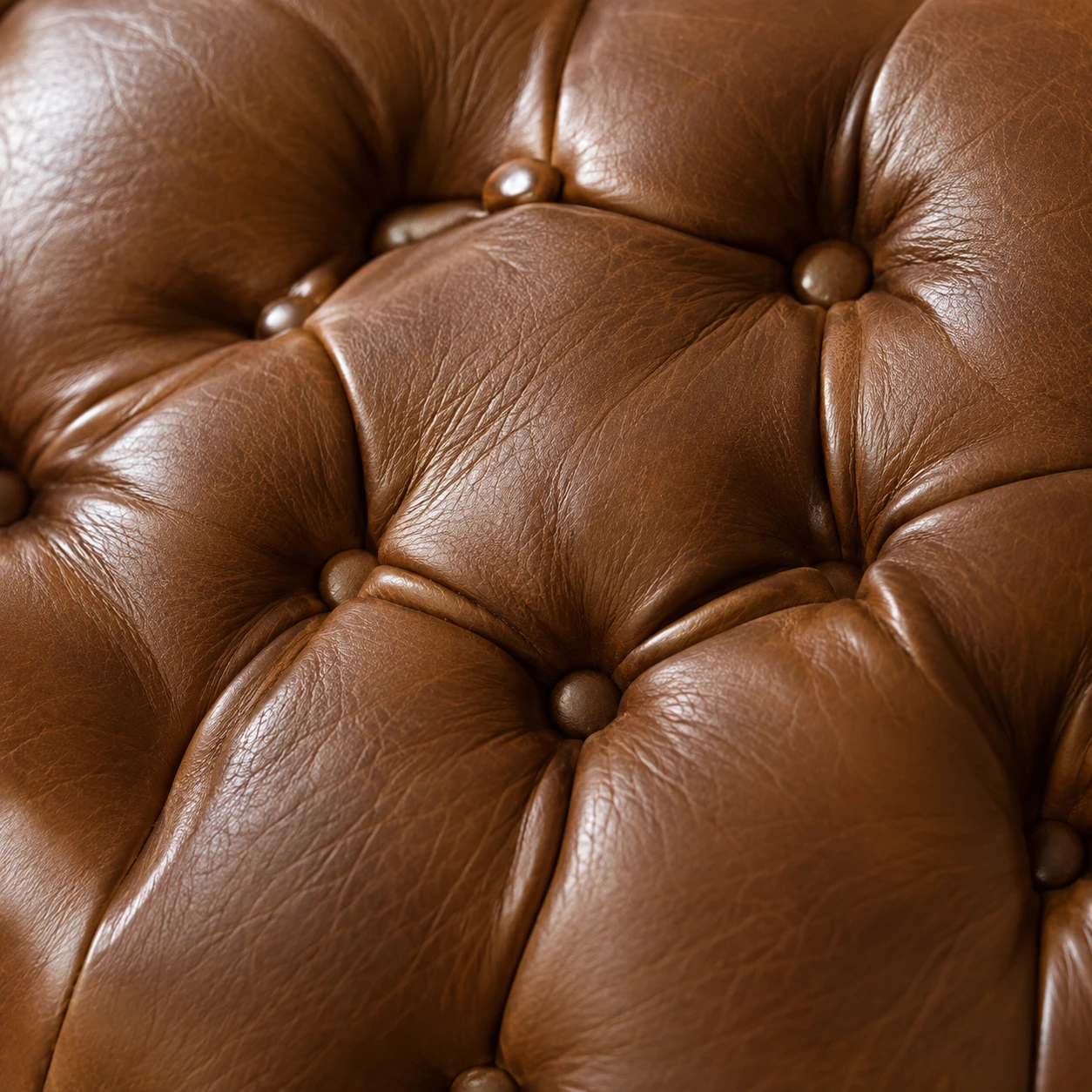 A close view of deep buttoned tufting in warm brown leather, each button drawn into the hide by hand