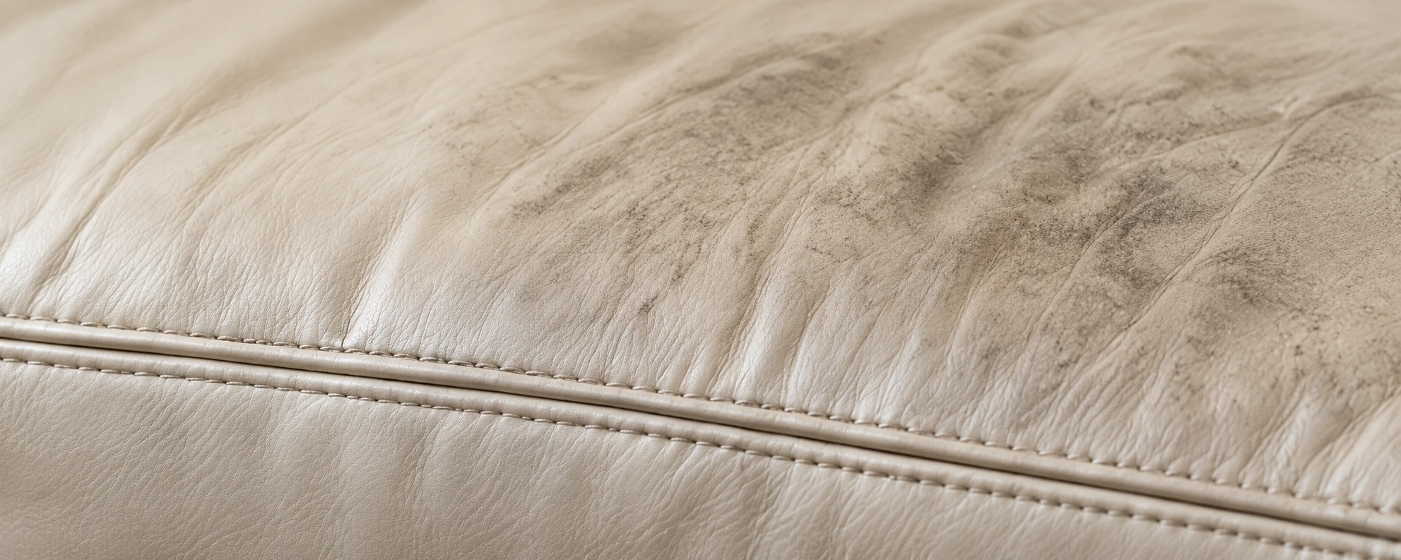 A cream leather cushion with grey surface soiling across the top