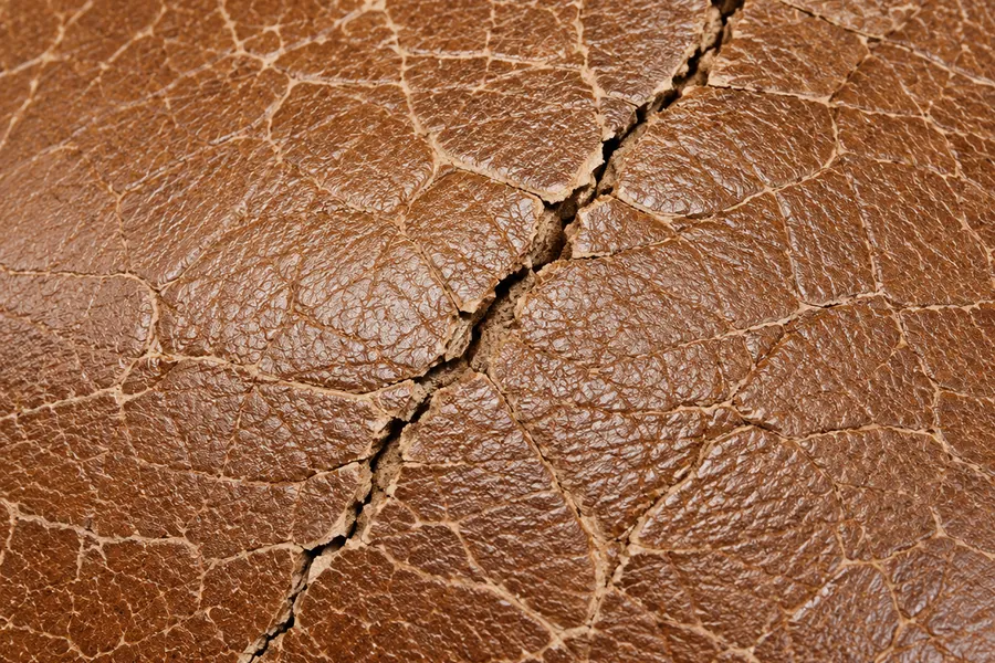 Dry tan leather split open along a hardened crack line
