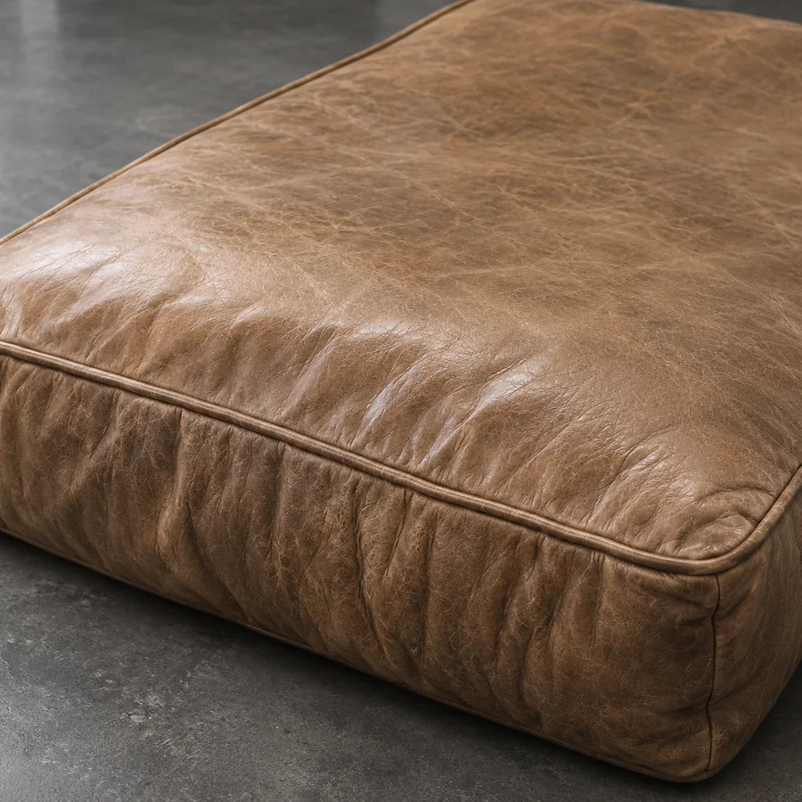 Tan leather seat cushion lying on a concrete floor with almost no loft left in it