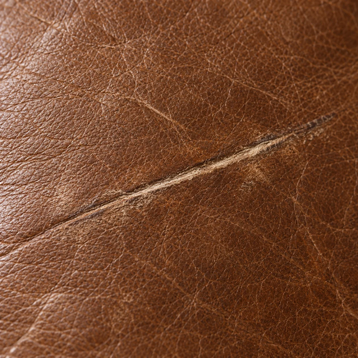 Scratch scored across the grain of a brown leather cushion