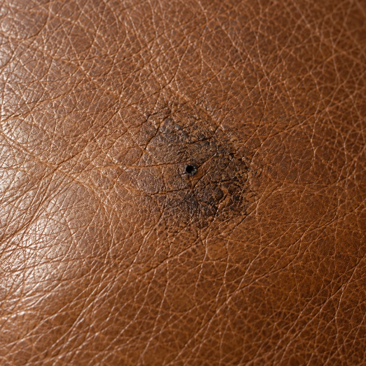 Dark stain soaked into the surface of a brown leather cushion