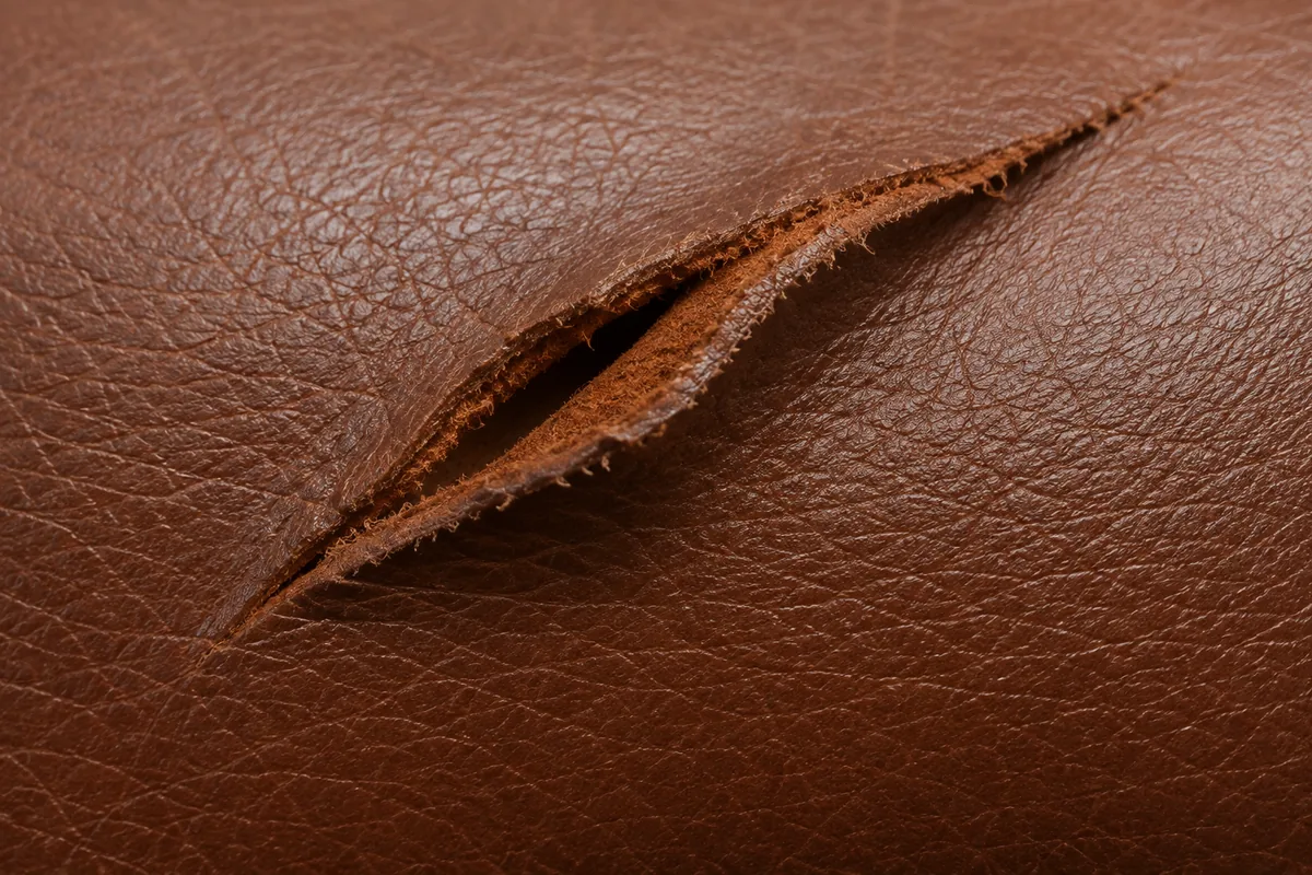 Clean slit cut through brown leather showing the pale fibre inside