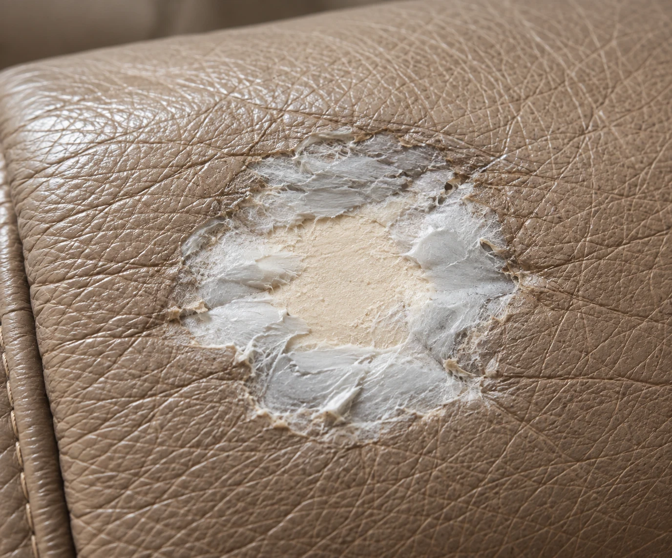 Pale flexible filler packed around an opening in taupe leather over a backing patch