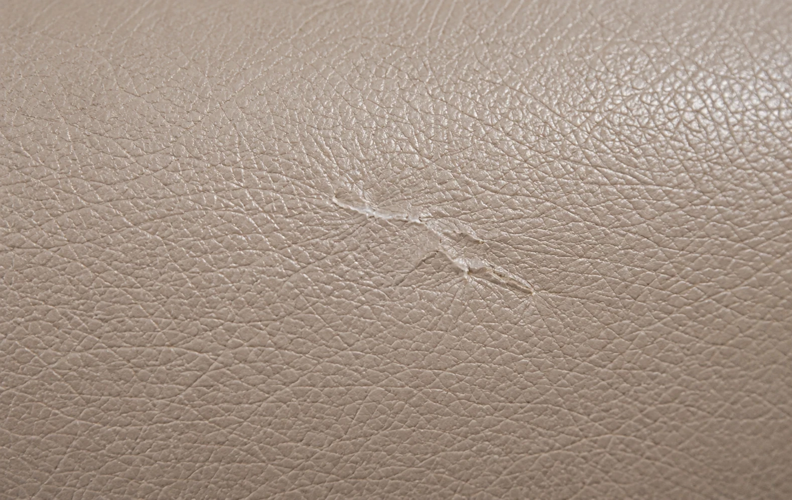 Levelled filler showing as a low ridge in taupe leather while the grain is rebuilt