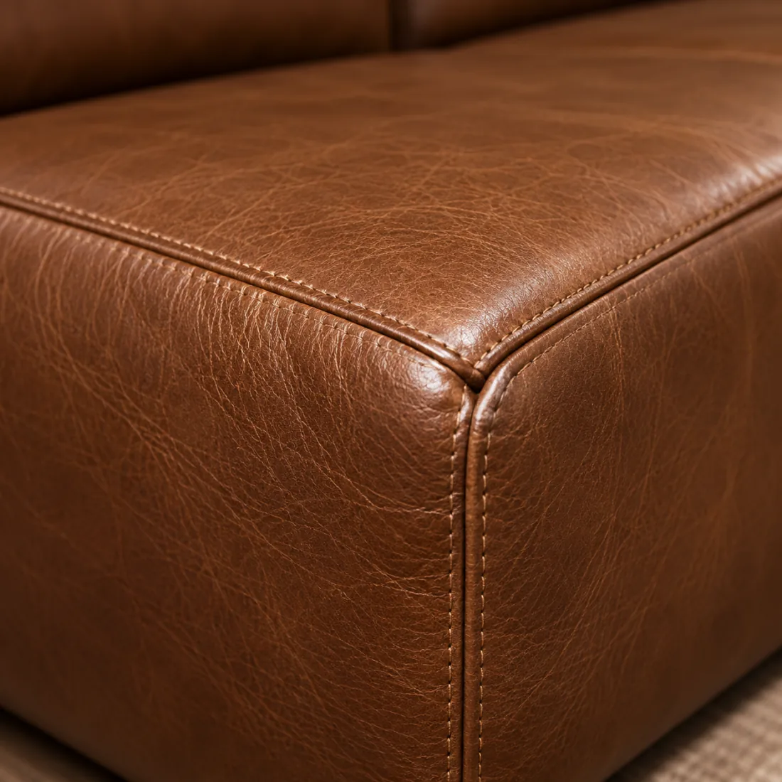 The front corner of a brown leather sofa arm, two panels stitched together down the curve
