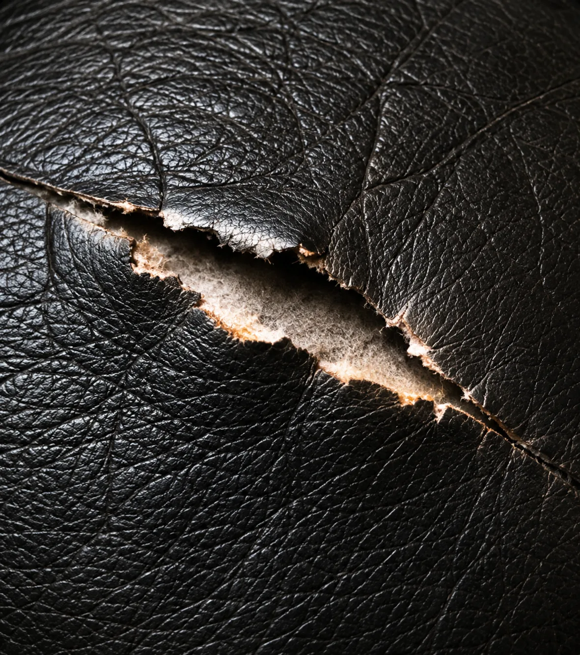 A rip in a black leather cushion with a pale wadding layer visible through the opening