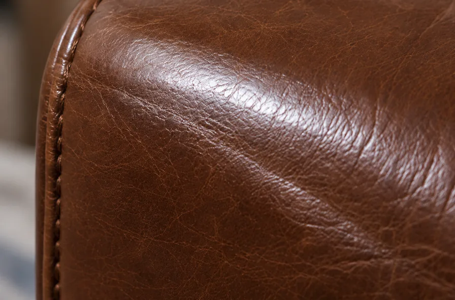 The crown of a brown leather arm with a polished band throwing back more light than the matte grain around it