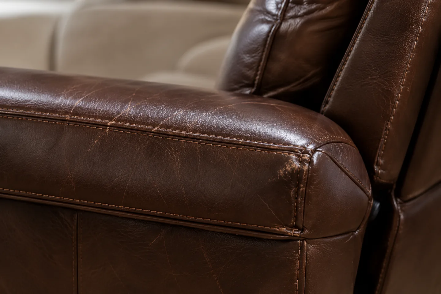 The front corner of a brown leather armrest rubbed pale where hands and sleeves cross it