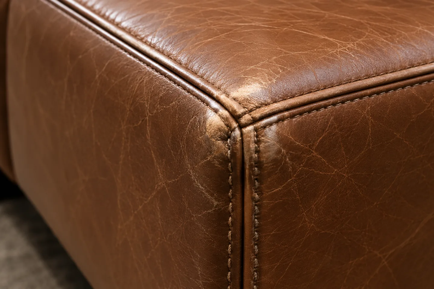 The rolled front corner of a tan leather seat cushion burnished lighter than the panel