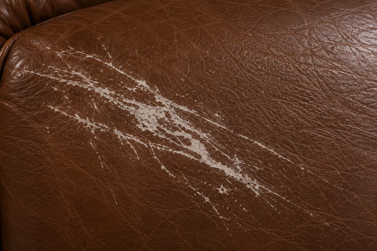 Pale abrasion streak across a brown leather arm where the protective topcoat has been scraped away