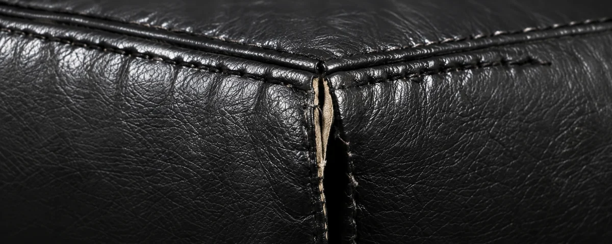 A black leather backrest corner opened at the seam, pale batting pushing out of the gap