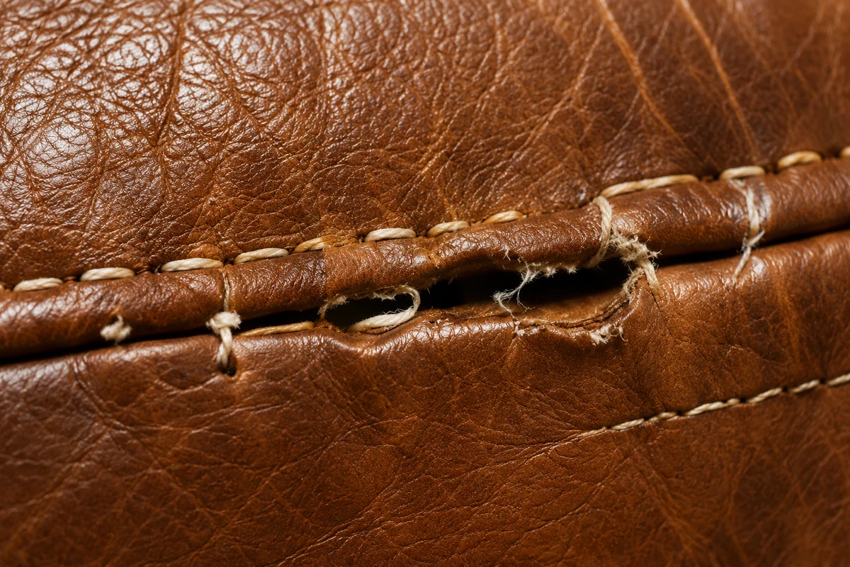 Tan leather seam with the cream topstitching frayed and pulled clear, leaving a small dark gap between the panels