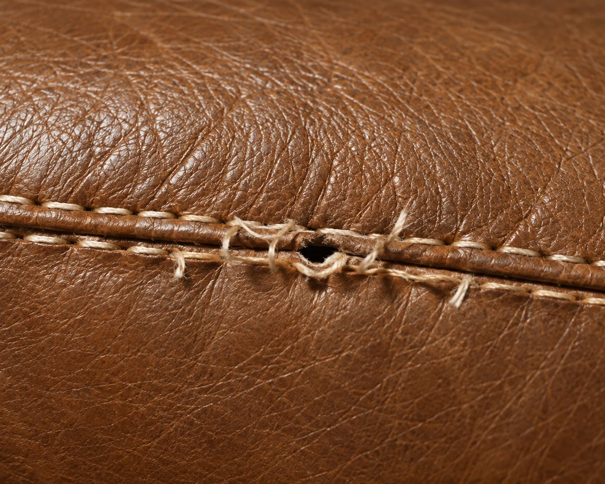 A twin-stitched brown leather seam where the thread has frayed and a stitch hole has opened into the hide