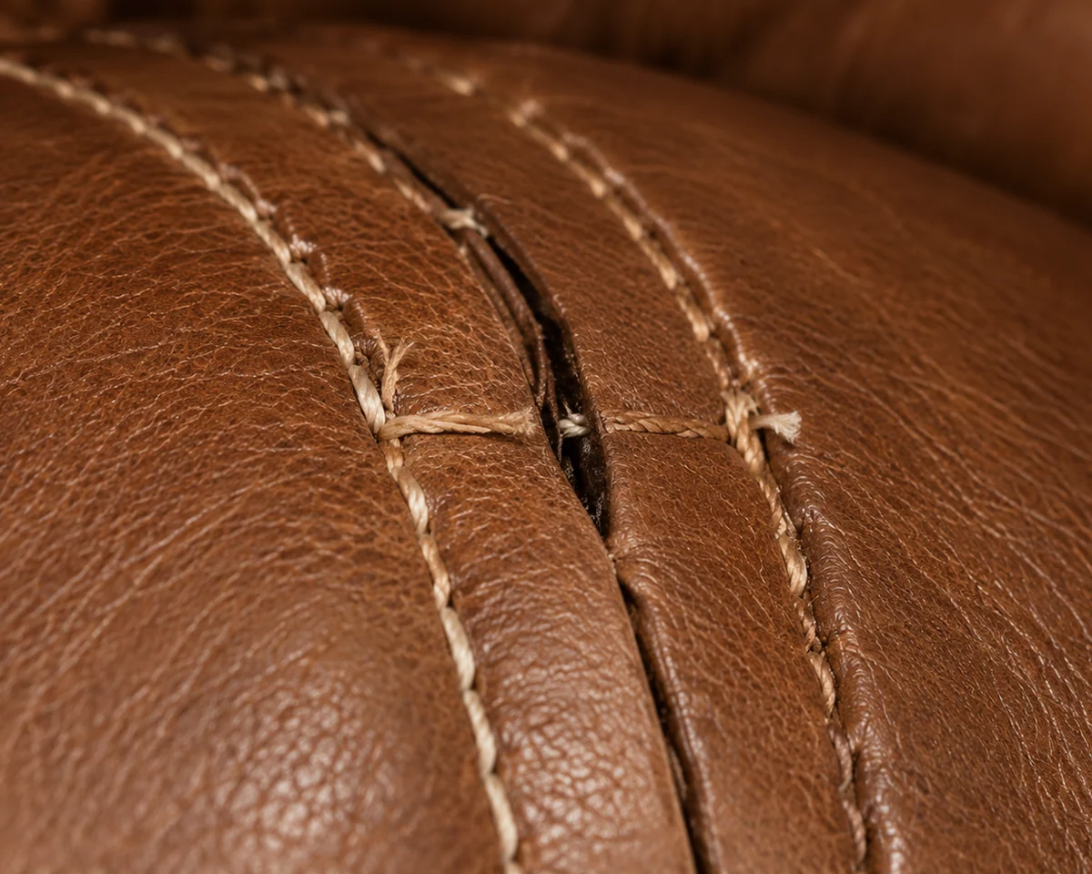 Two long parallel stitch lines running down a tan leather sofa arm, one broken open partway along