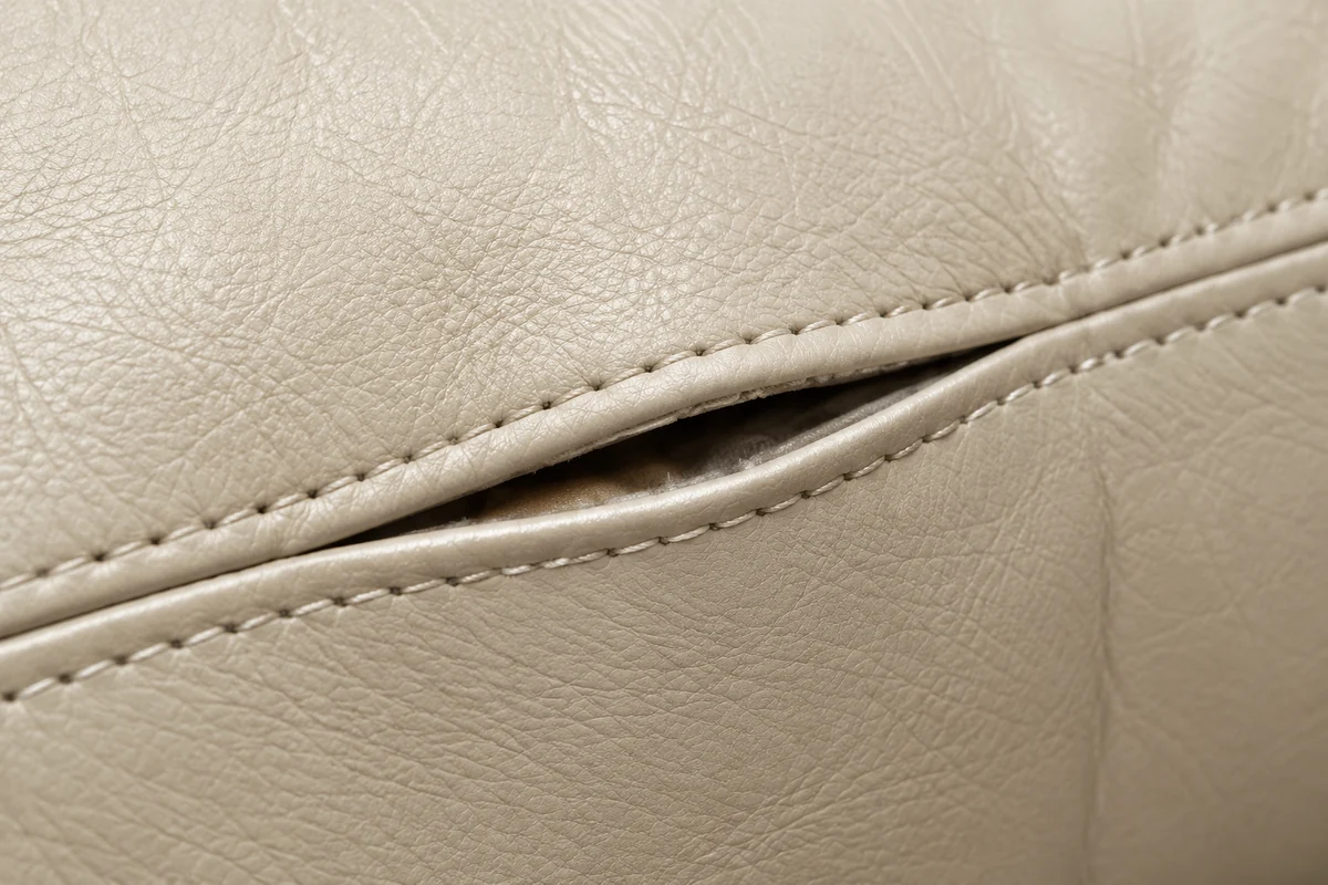 A cream leather cushion seam parted along a curve, the pale fill just visible inside the opening