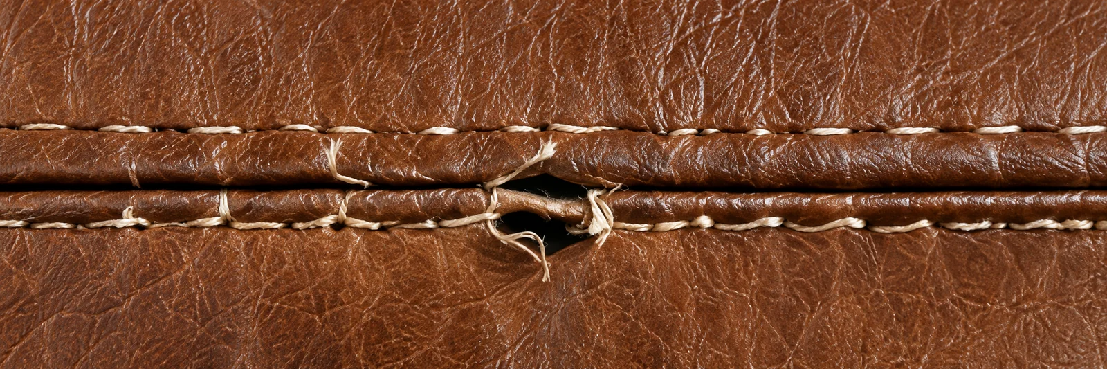 A brown leather seam where the thread has broken at one point, the leather either side clean and unmarked