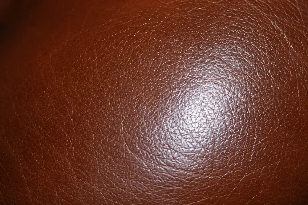 Reddish-brown leather catching a highlight, showing how sheen level changes the way a panel reads
