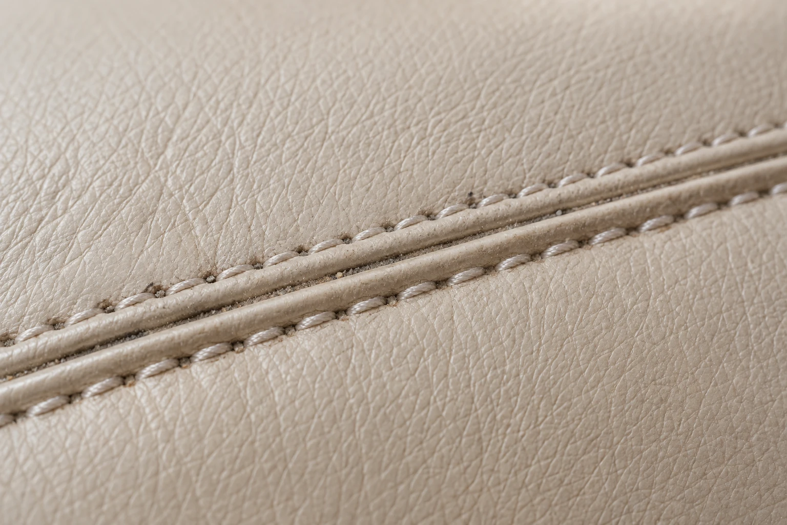 Dust packed into the double stitching of a beige leather seam