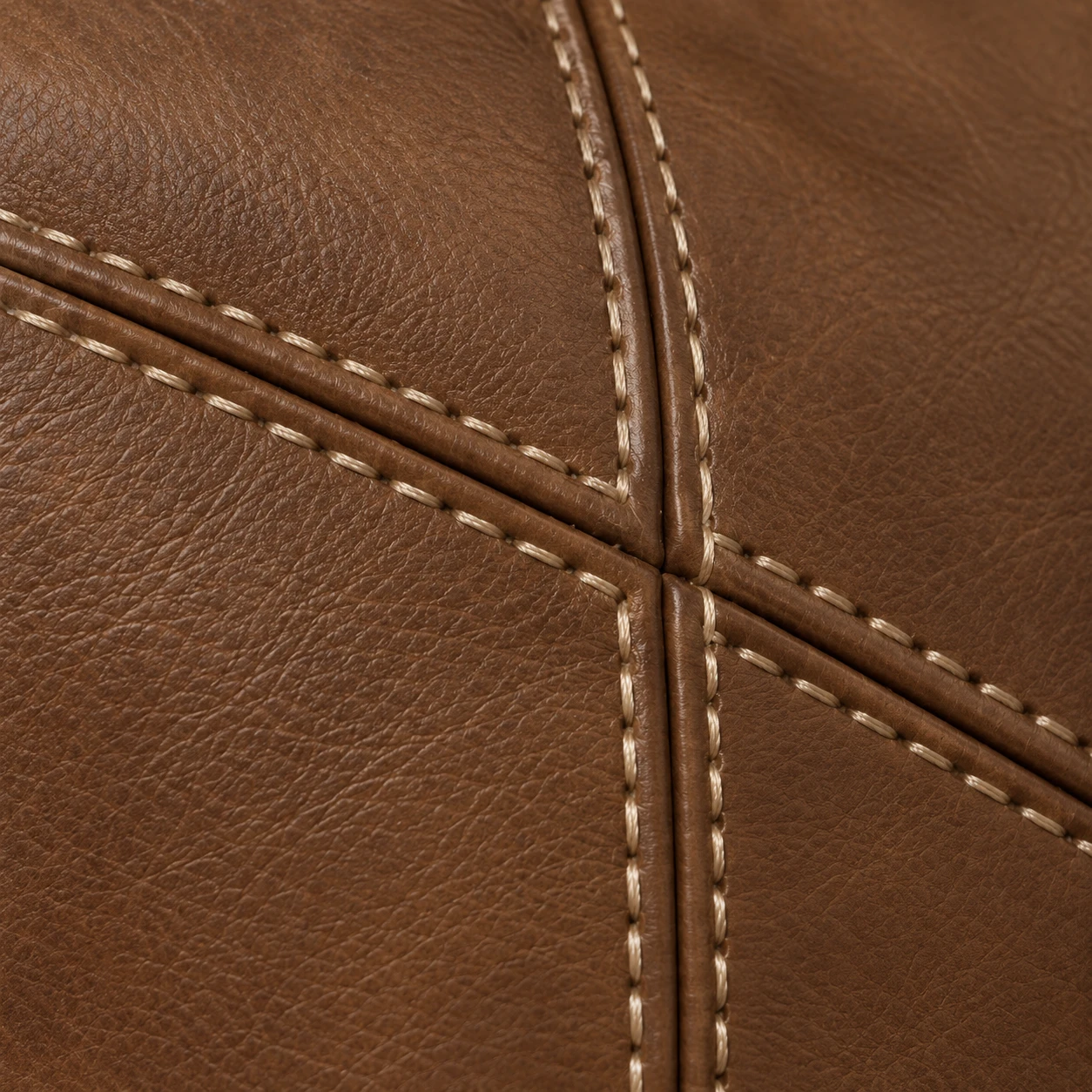 Close-up of tan leather with cream contrast stitching running along two seams that meet in a cross