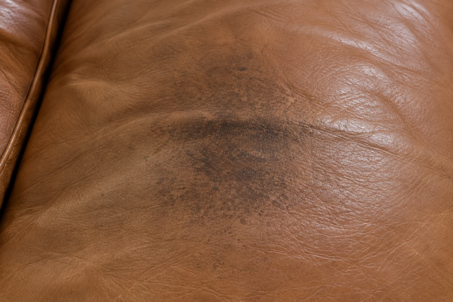 A dark oil patch soaked into the surface of a tan leather cushion