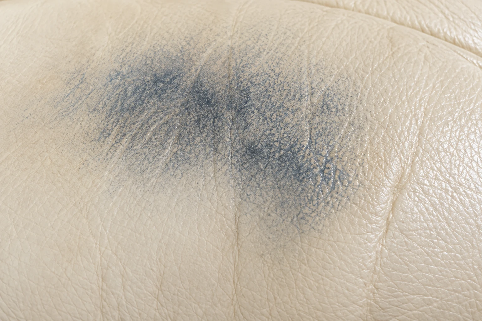 A diffuse blue-grey denim dye mark spread across cream leather