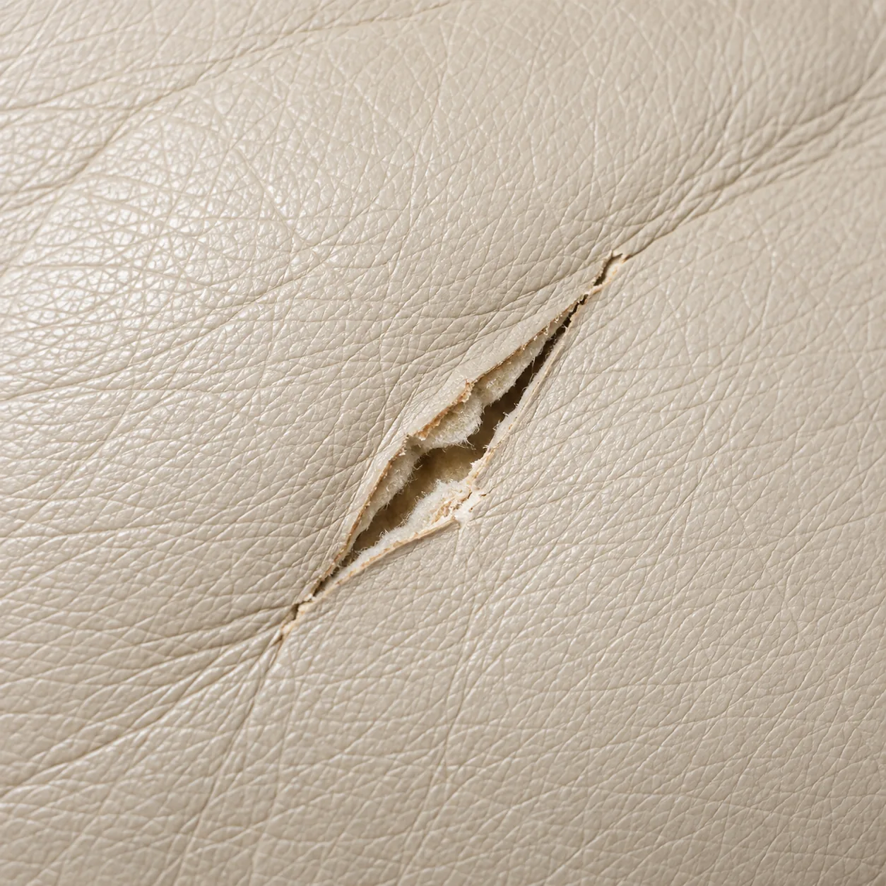A tear in a cream leather cushion: a narrow slit whose edges still line up